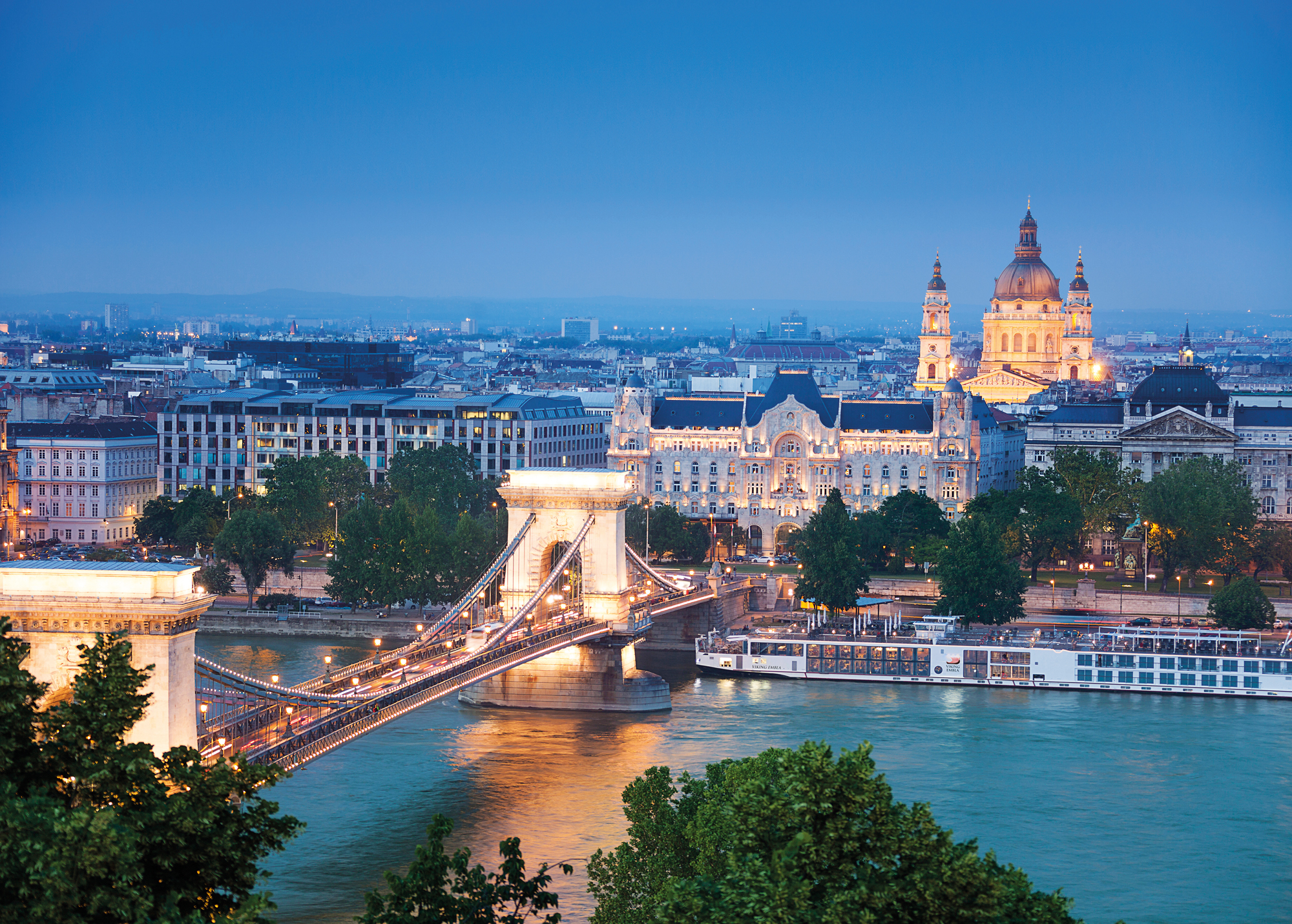 Viking Longship docked along the Danube River with Chain Bridge, St. Stephen's Basilica illuminated in the evening in Budapest, Hungary.